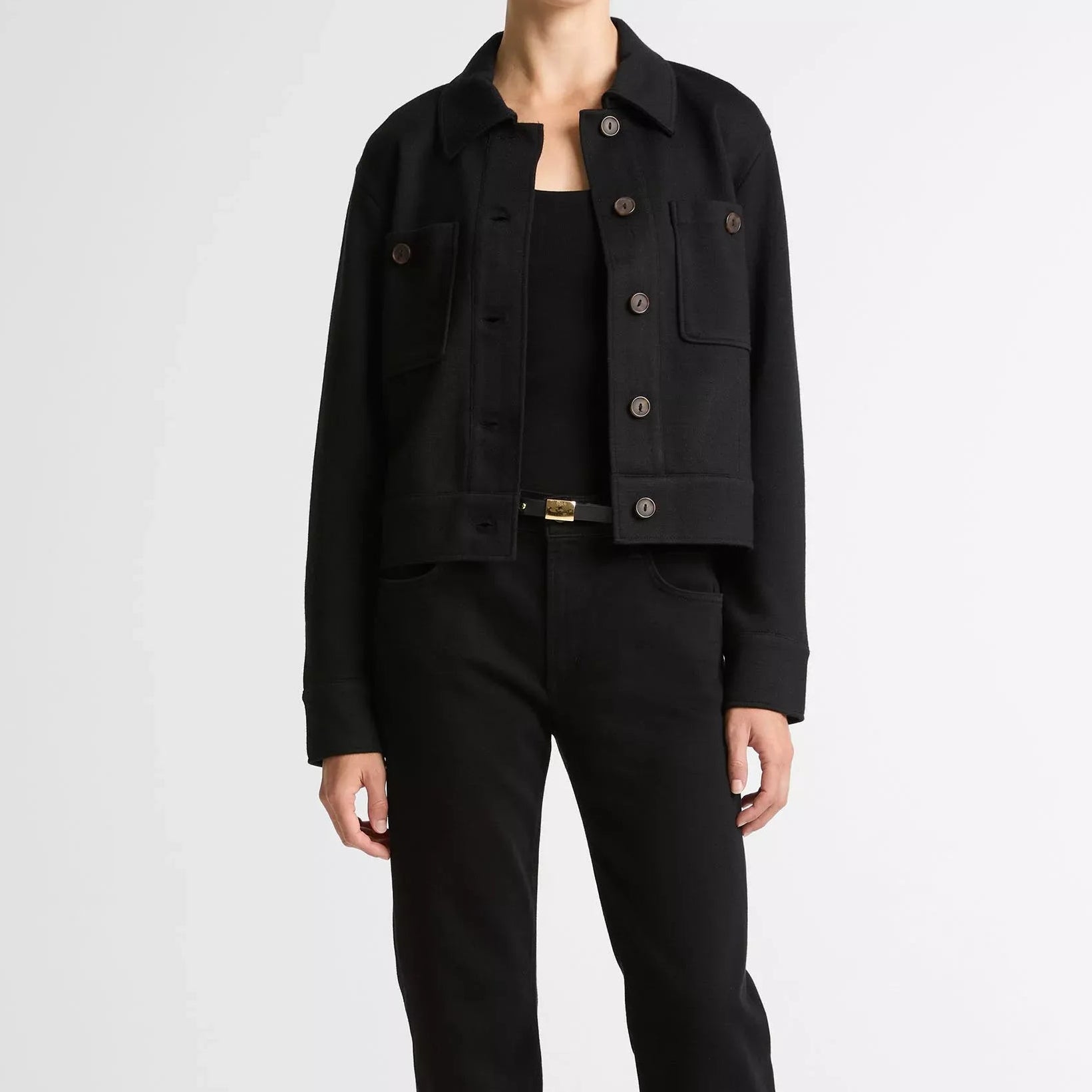 Rear view of a model wearing a black tailored blazer with three-quarter sleeves and matching black trousers against a plain light gray studio background.