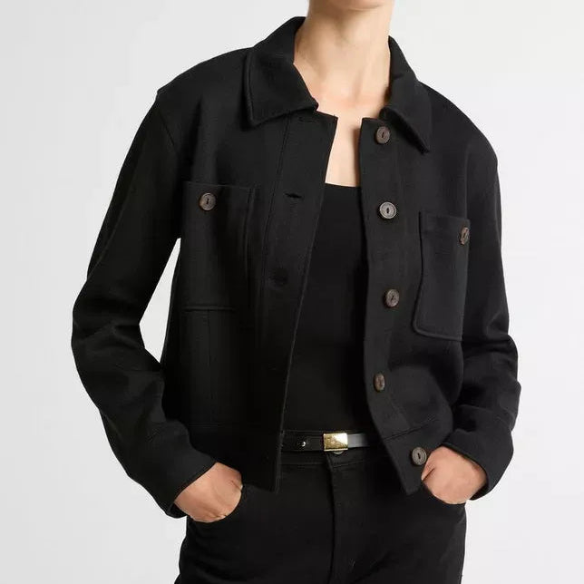 A model wearing a black cropped utility jacket with dark buttons, paired with black pants and a black top, against a light gray studio background.