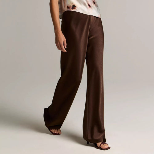 A model shown from the back wearing a textured light beige knit sweater and matching tan wide-leg trousers against a plain light gray studio background.