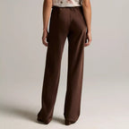 A model shown from the back wearing a sleeveless top with a white base and brown floral pattern, paired with high-waisted brown wide-leg trousers, against a neutral light gray studio background.