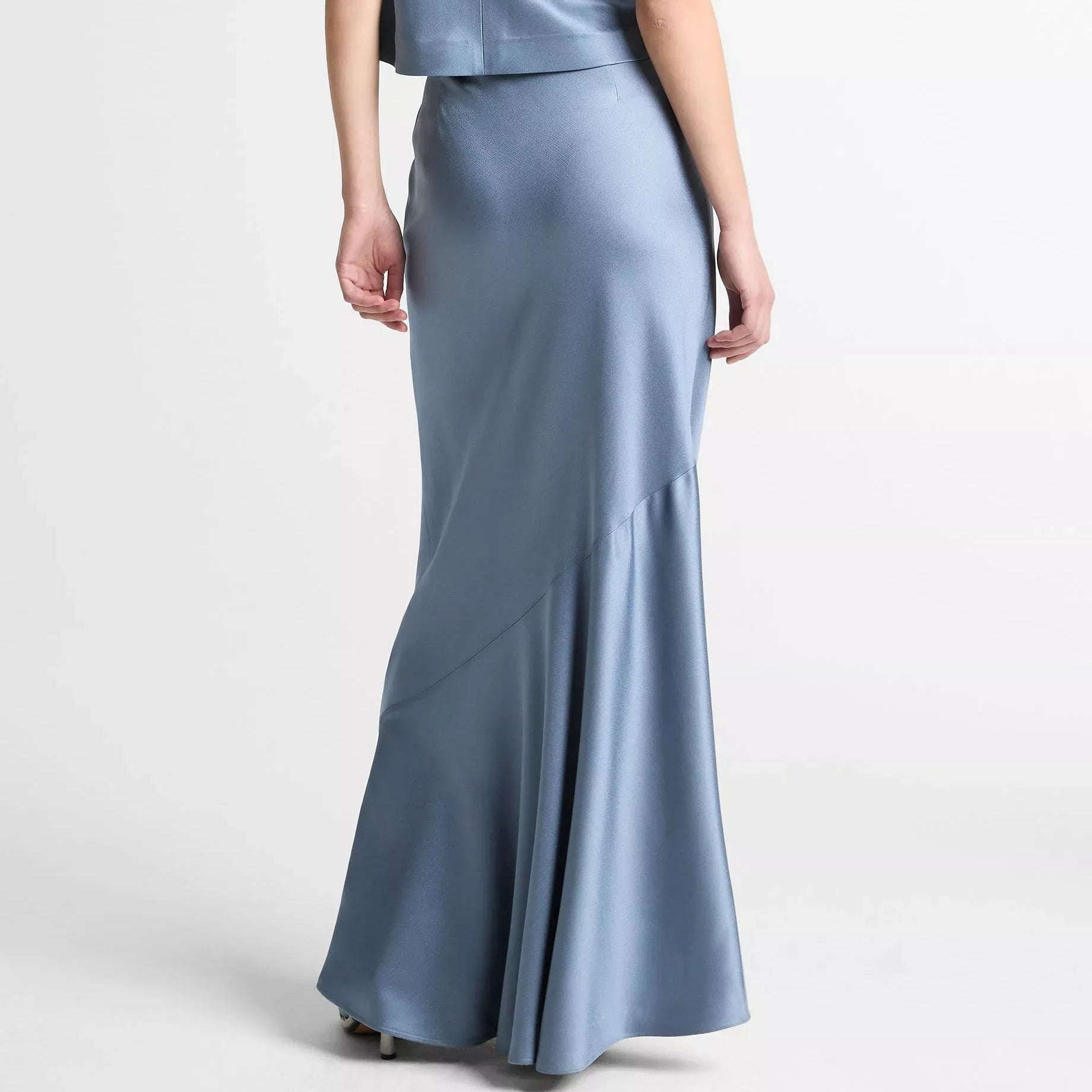 A model shown from the back wearing a sleeveless cream jumpsuit with wide-leg trousers and a high waist, set against a plain light gray studio background.