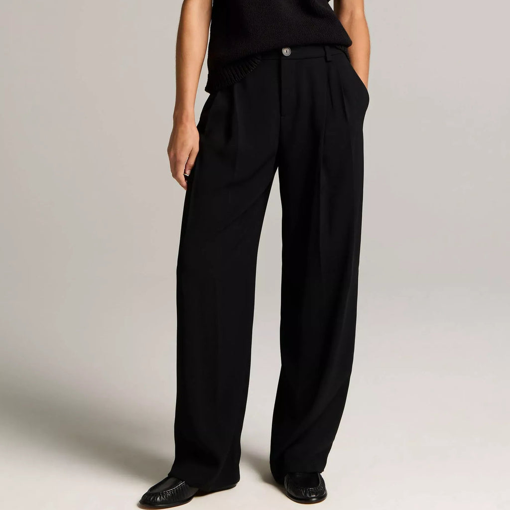 A model wearing a cream-colored sleeveless top and matching wide-leg trousers with a drawstring waist, photographed against a neutral light gray studio background.