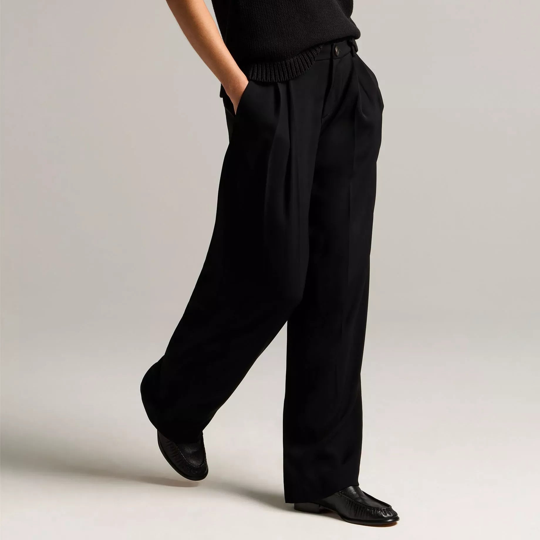 A model wearing a light beige sleeveless top and matching wide-leg trousers with a tie waist, styled with beige heeled sandals against a neutral studio background.