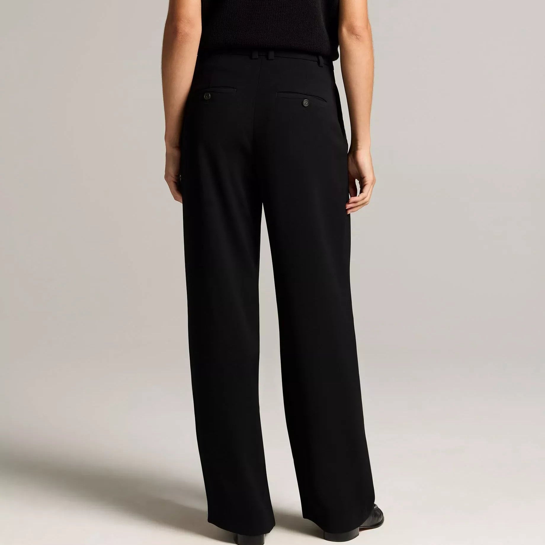 A model shown from the back wearing a sleeveless cream-colored top and matching wide-leg trousers, photographed against a neutral light gray studio background.