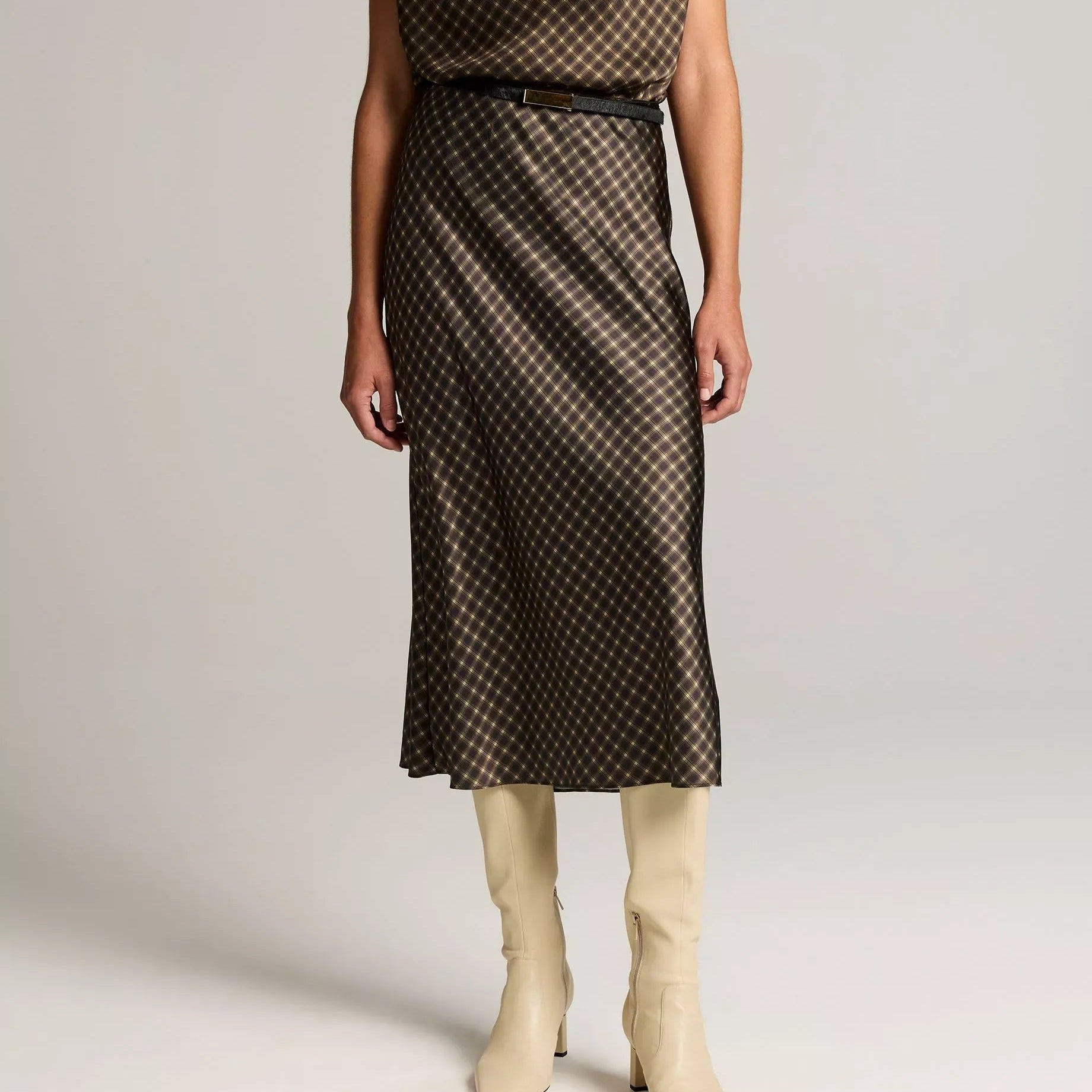 A model wearing a two-piece satin outfit in a dusty blue color, featuring a sleeveless mock-neck top and a matching long skirt, paired with light blue strappy sandals against a plain white studio background.