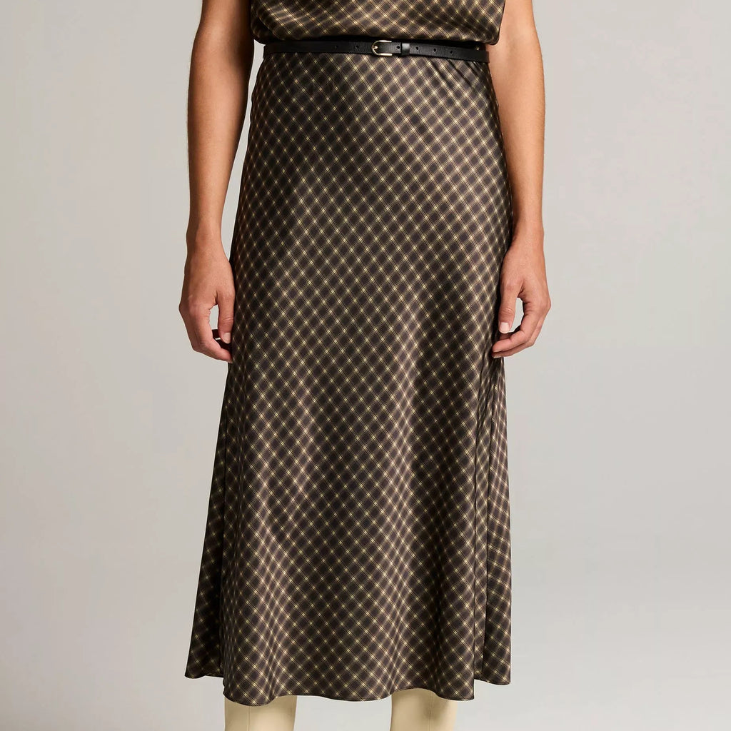A model wearing a brown and beige patterned midi skirt with a thin black belt, paired with beige ankle boots, against a light gray studio background.