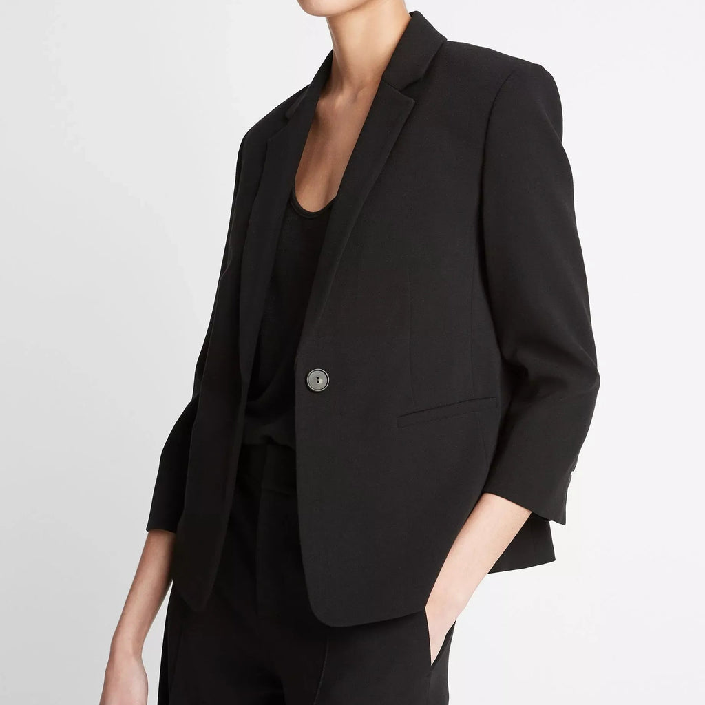 Person wearing a black blazer and pants on a light gray background