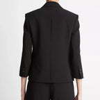 Rear view of a model wearing a black tailored blazer with three-quarter sleeves and matching black trousers against a plain light gray studio background.