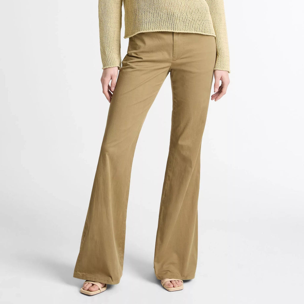 A model wearing a black sleeveless knit top and matching black wide-leg trousers, standing against a neutral light gray studio background.