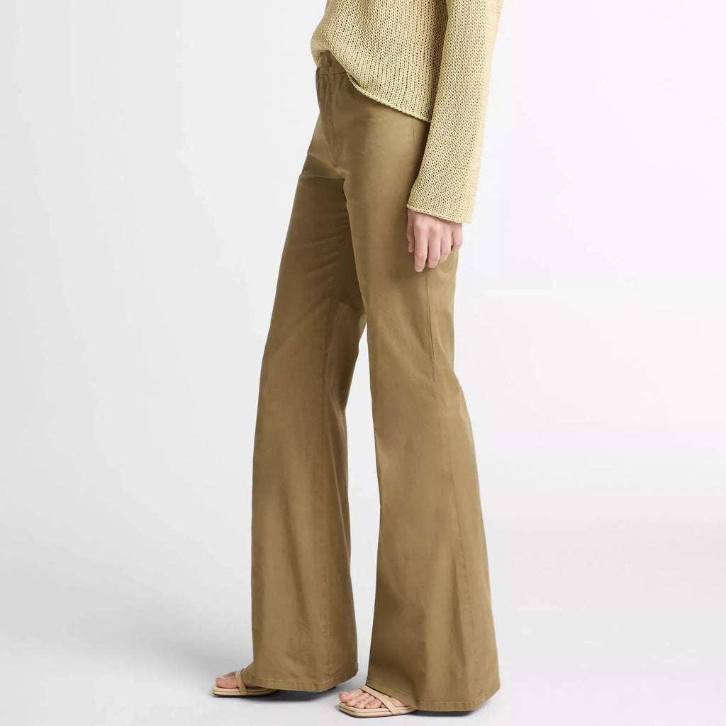 A model shown from the side wearing a light beige knit sweater and matching wide-leg trousers in a warm khaki shade, paired with beige flat sandals, against a plain white studio background.