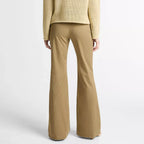 A model shown from the back wearing a textured light beige knit sweater and matching tan wide-leg trousers against a plain light gray studio background.