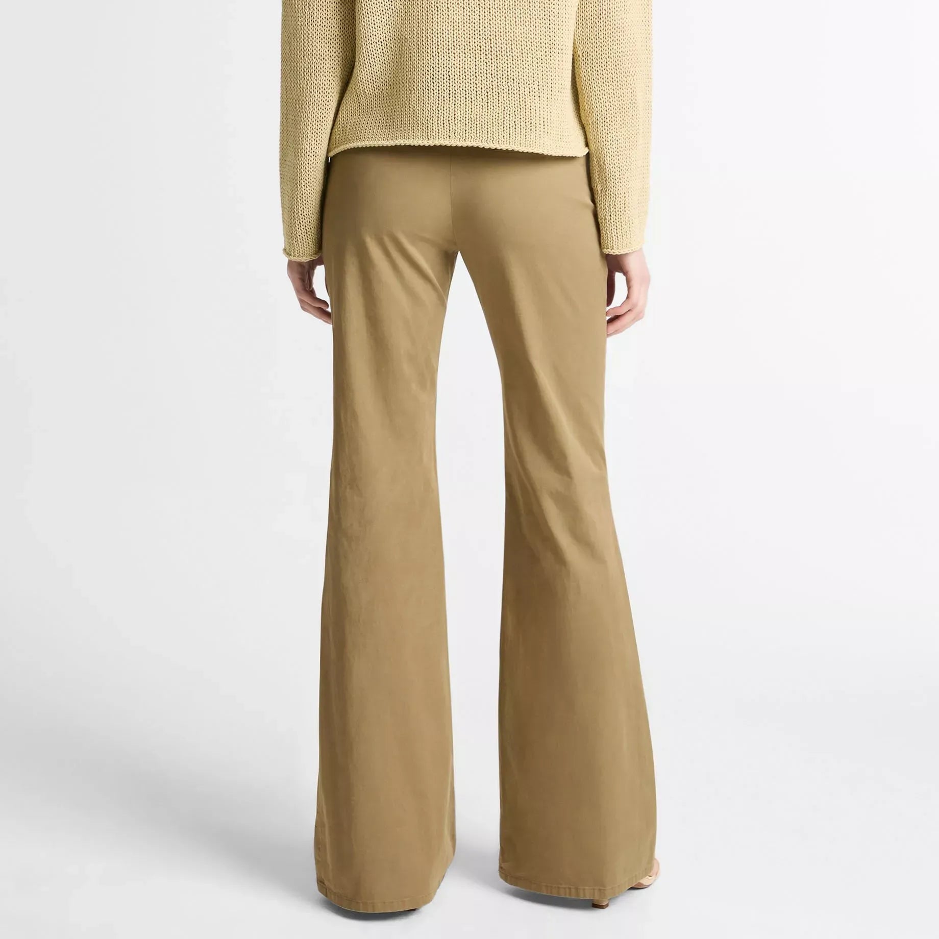 A model shown from the back wearing a textured light beige knit sweater and matching tan wide-leg trousers against a plain light gray studio background.