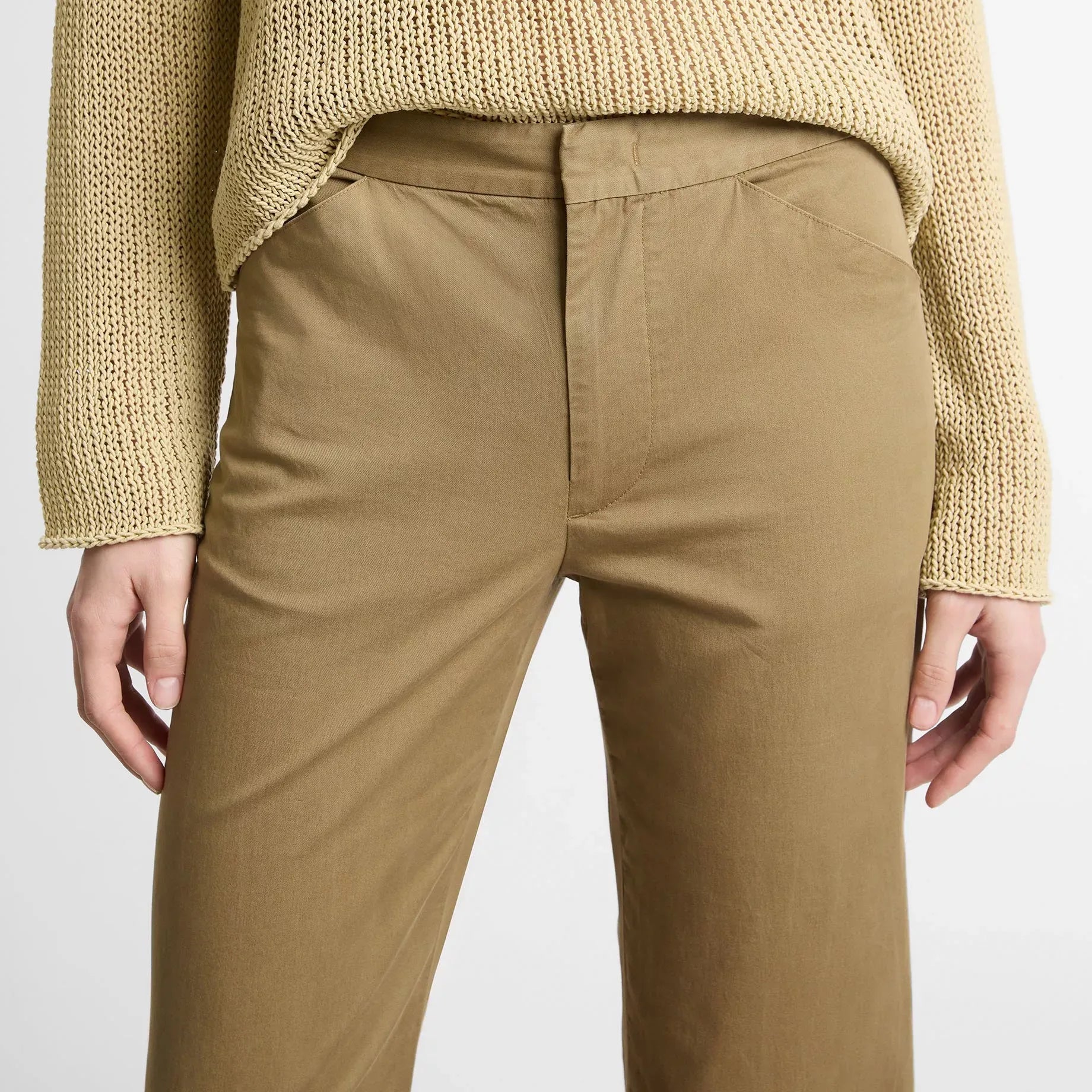A person wearing a chunky knit sweater in a warm beige/cream tone and tailored trousers in a camel brown color, shown from the chest down against a plain light background.