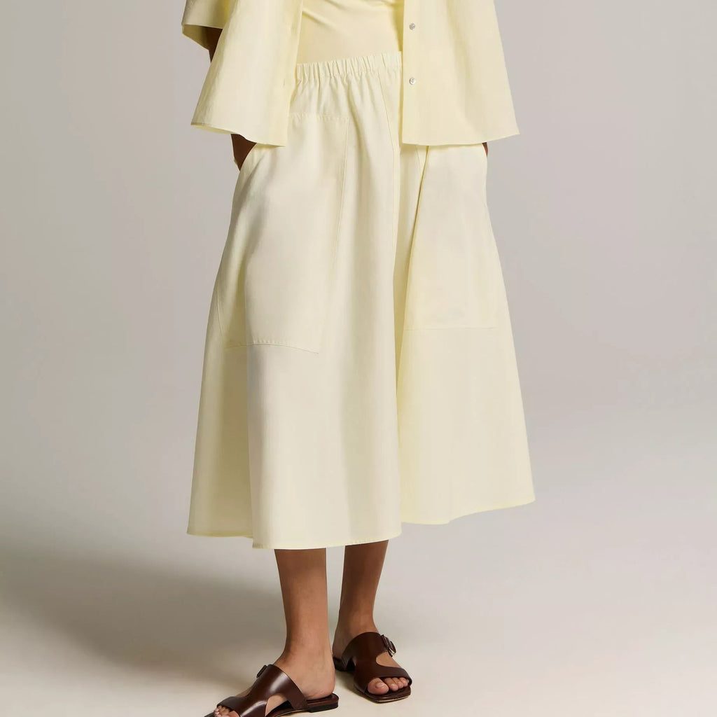 A model wearing high-waisted, wide-leg brown trousers paired with a sleeveless floral top and flat sandals, shown from the chest down against a neutral studio background.