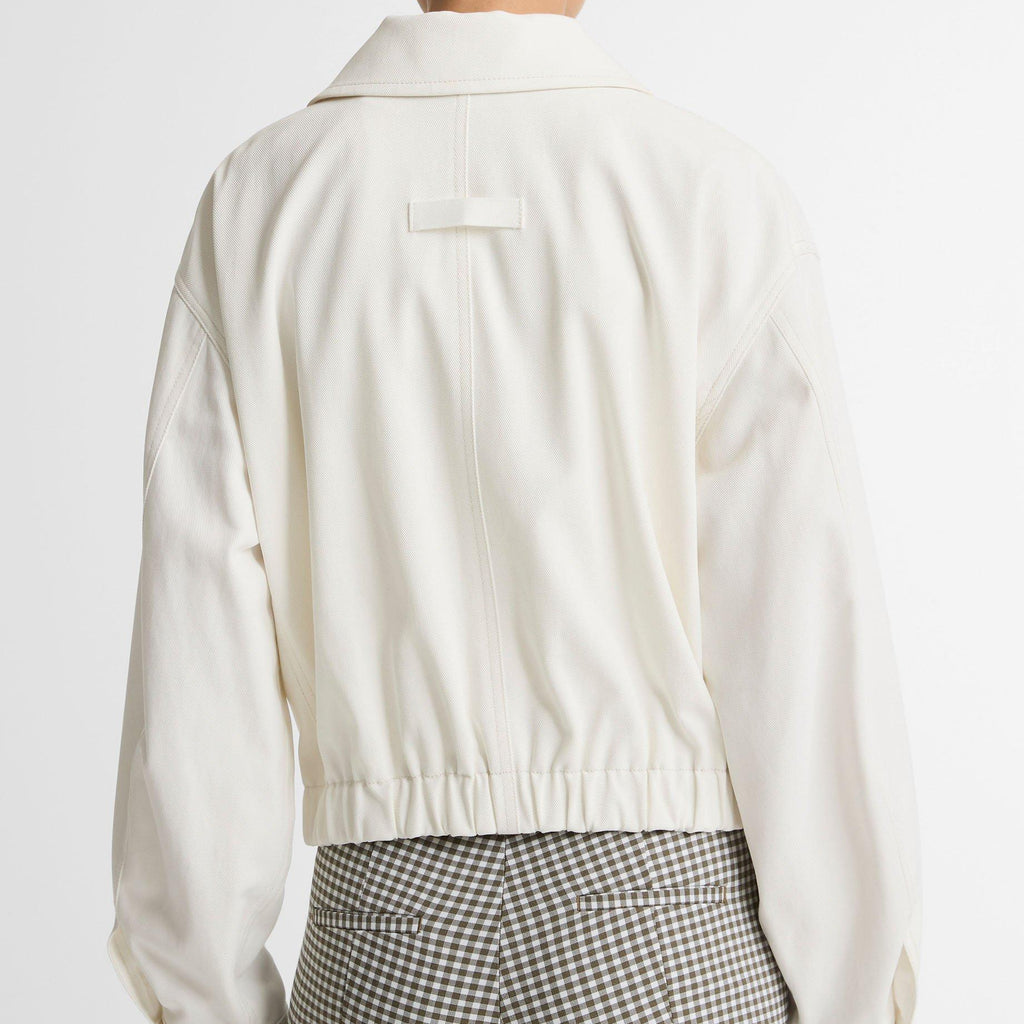 Back view of a person wearing a cream cropped jacket and gray-and-white gingham trousers, photographed against a plain light background.