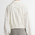Back view of a person wearing a cream cropped jacket and gray-and-white gingham trousers, photographed against a plain light background.