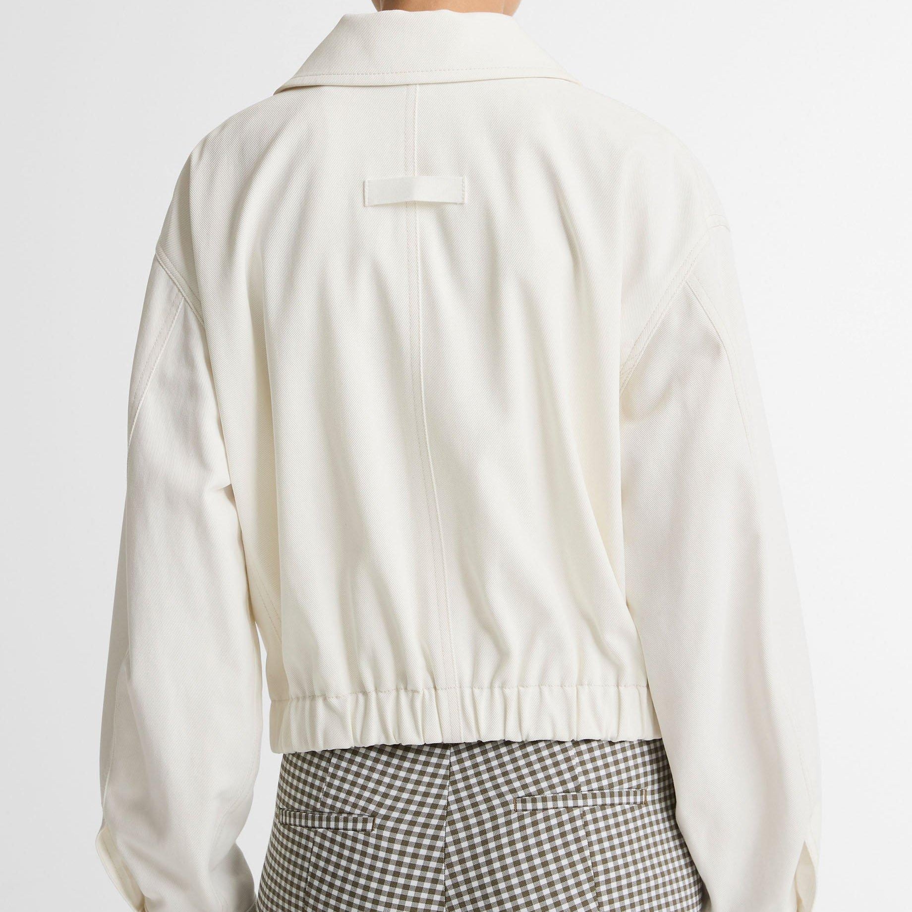 Back view of a person wearing a cream cropped jacket and gray-and-white gingham trousers, photographed against a plain light background.