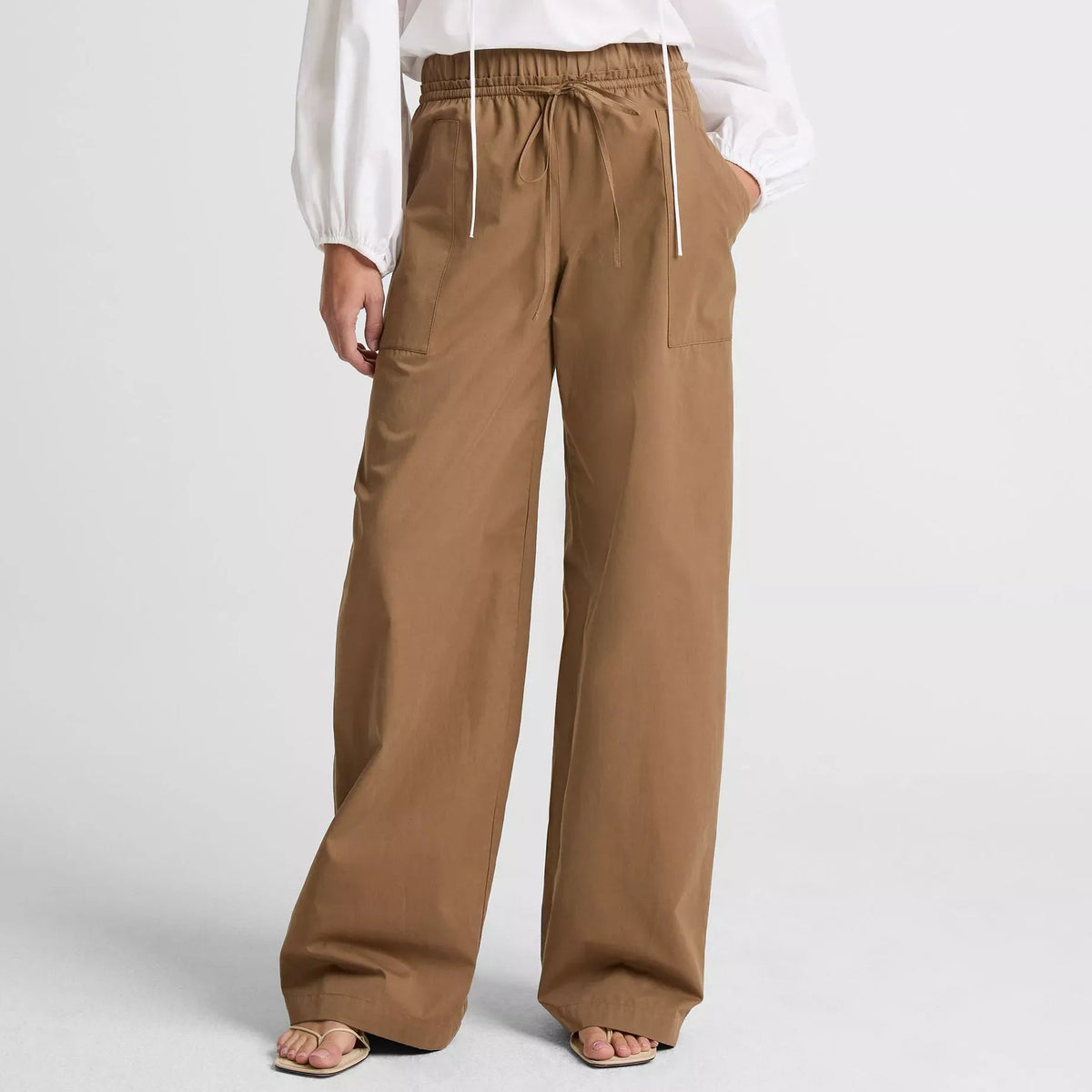 Person wearing a white blouse and brown wide-leg pants on a light gray background