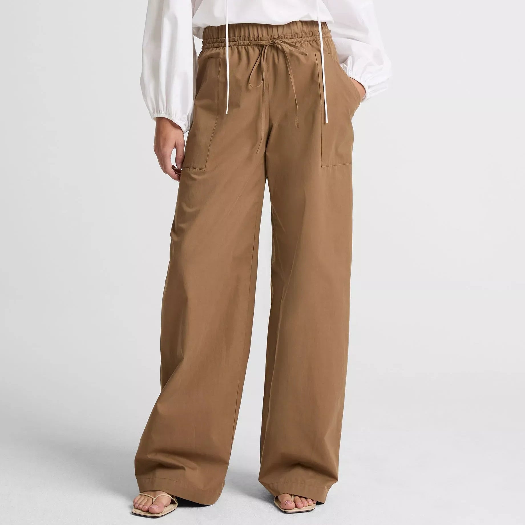 Person wearing a white blouse and brown wide-leg pants on a light gray background