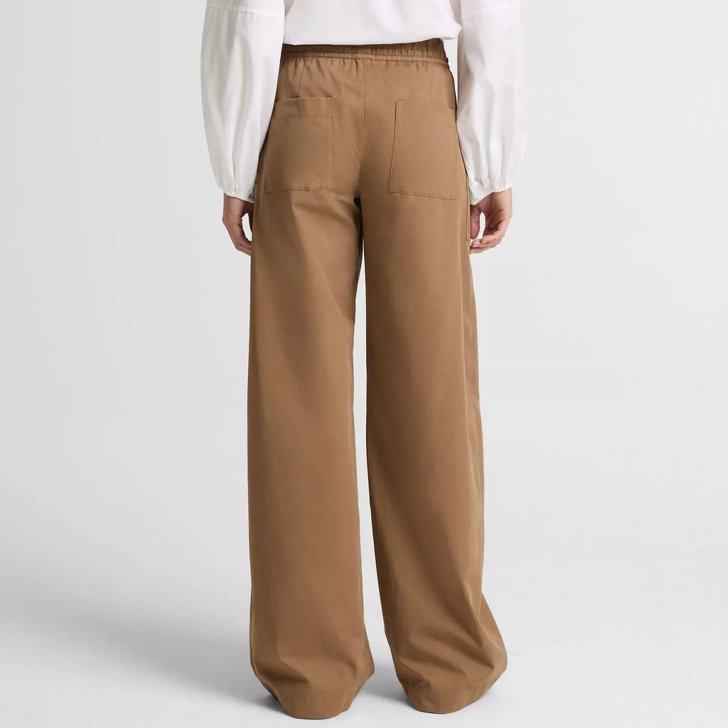 Person wearing a white blouse and brown pants on a light gray background