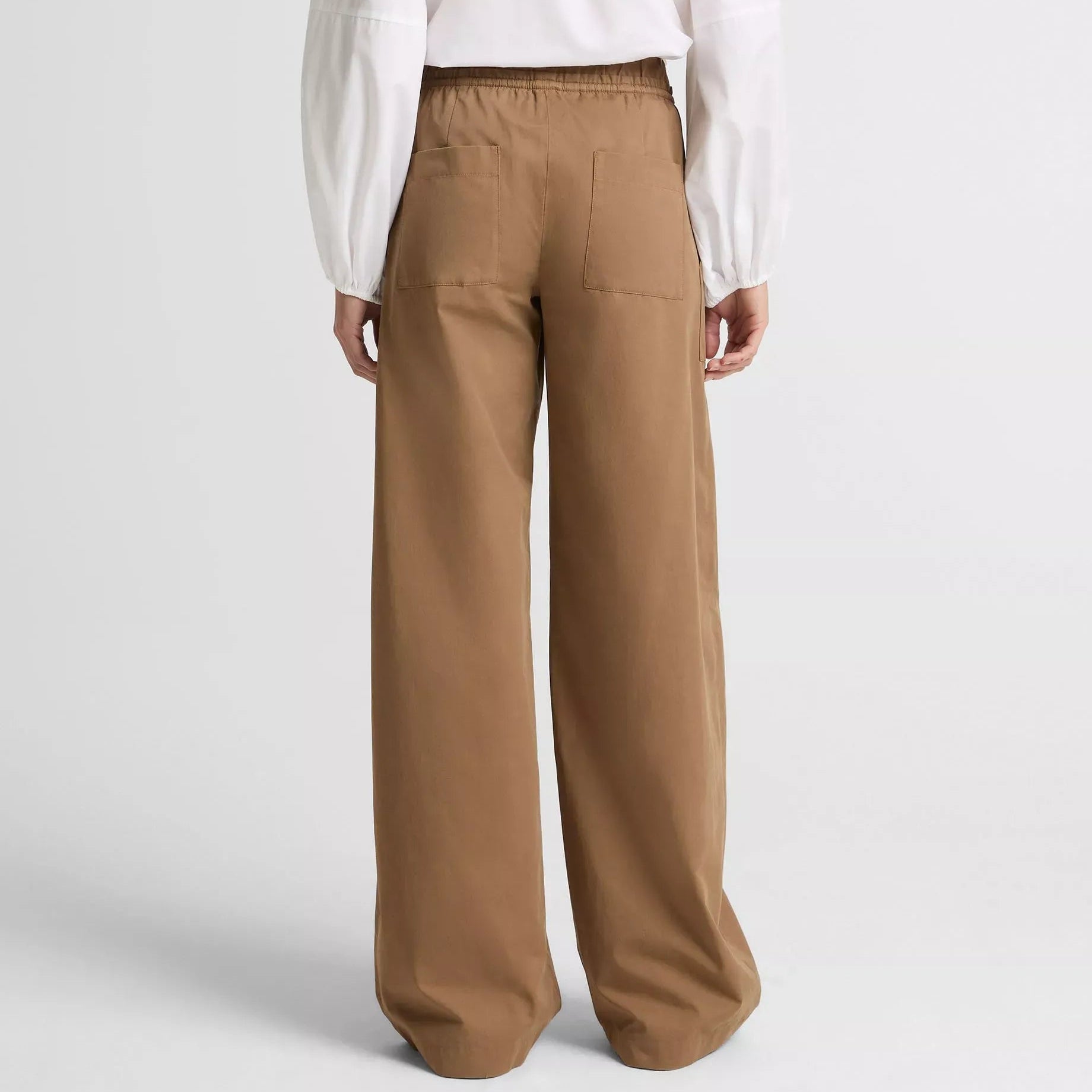 Person wearing a white blouse and brown pants on a light gray background