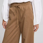 A person wearing brown wide-leg drawstring pants and a white long-sleeve blouse, shown from the chest down against a light gray studio background.